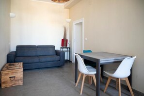 Ein modernes Wohnzimmer mit einem grauen Sofa, einer Holzbank und einem Esstisch mit weißen Stühlen.
