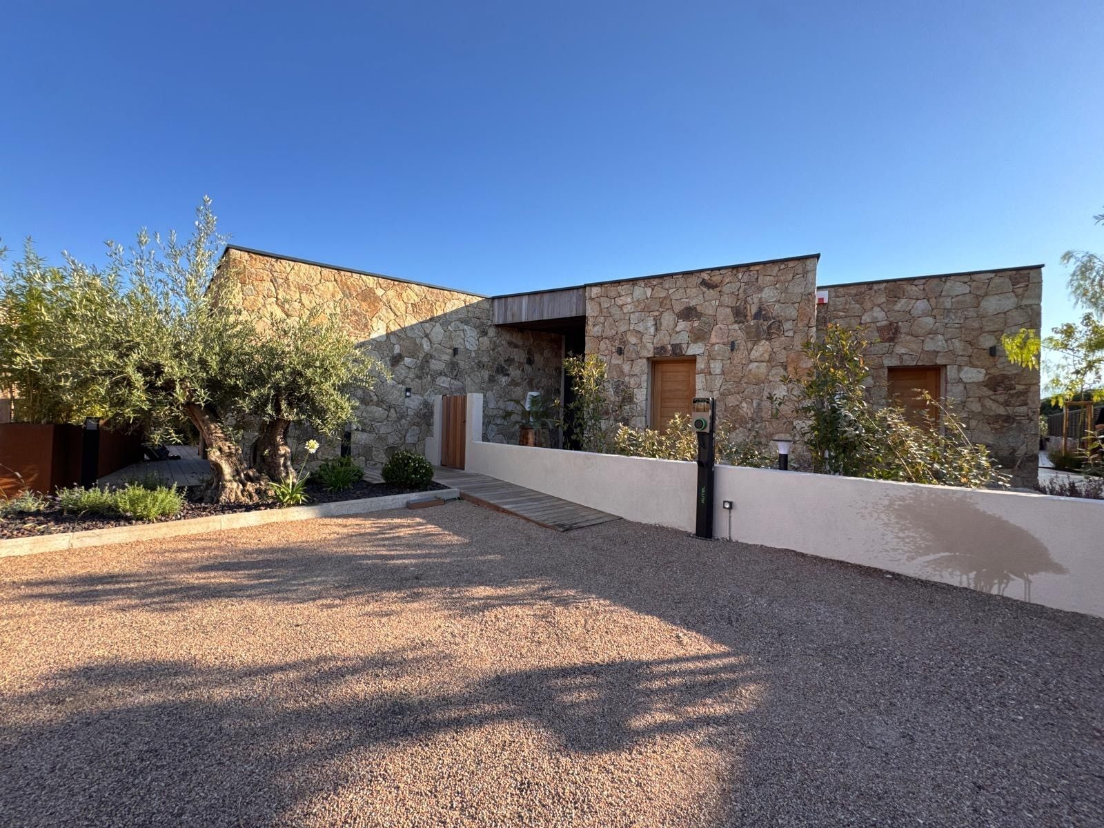 A modern house with a stone facade, a wooden door, and a gravel driveway.