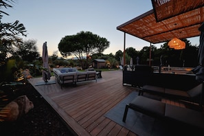 An outdoor deck with a sofa and chairs, surrounded by trees and a wooden pergola with hanging lights. - VILLA DOLCE VECCHIA—Exceptional Villa in Cala Rossa—Beach within walking distance, sleeps 10 (Lecci)