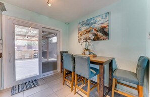 A dining area with a wooden table and four chairs, a painting on the wall, and a sliding glass door leading outside.