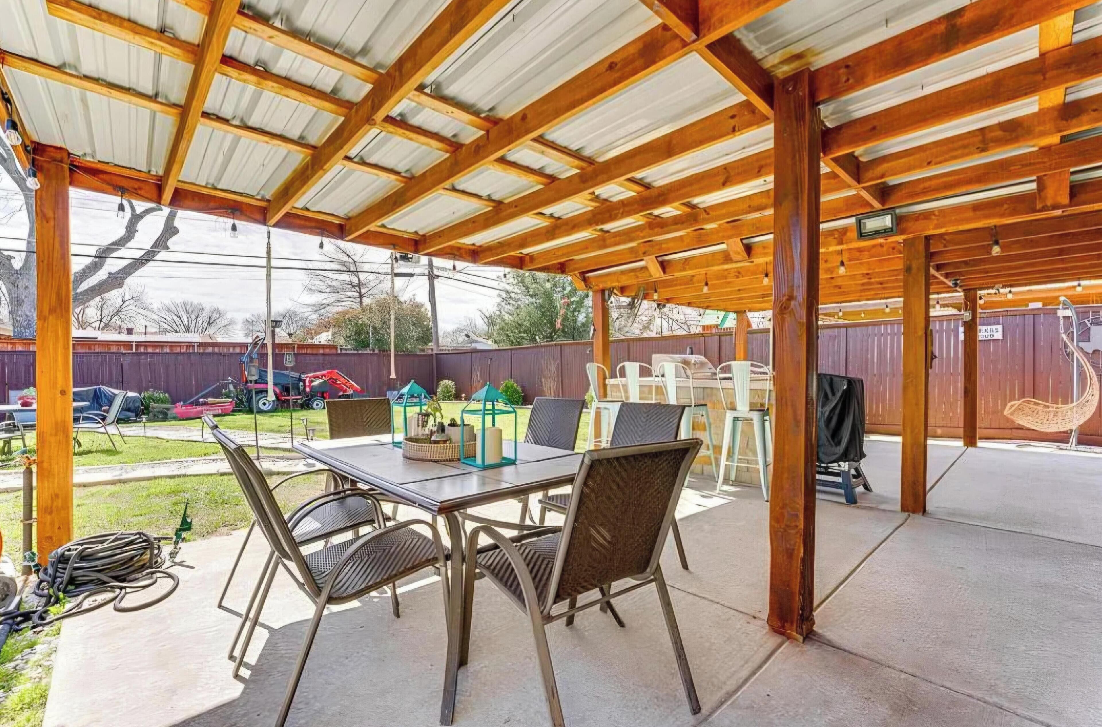 Une terrasse extérieure dotée d’une pergola en bois, d’une table avec des chaises et d’un espace abrité offrant une vue sur le jardin arrière.