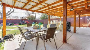 Een terras buiten, met een houten pergola, een tafel met stoelen en een overdekt gedeelte met uitzicht op de achtertuin.