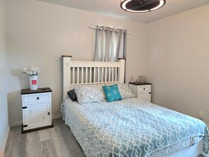 A bedroom with a bed, nightstands, a dresser, a window with curtains, and a ceiling fan.