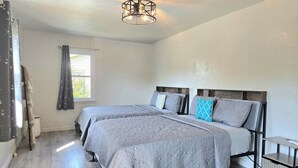 Een slaapkamer met twee bedden, een raam met gordijnen, een plafondlamp en een klein nachtkastje.