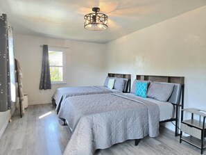 Ein Schlafzimmer mit zwei Betten, einem Fenster mit Vorhängen, einer Deckenleuchte und einem kleinen Nachttisch.