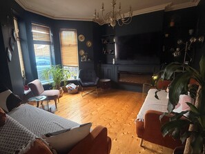 A living room with a fireplace, wooden flooring, and a large window with blinds. - Hens/Stags | Families | Corp | 14 guests £39pp (Cardiff)