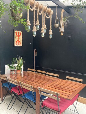 A dining area with a long wooden table, chairs, hanging macramé light fixtures, and potted plants. - Hens/Stags | Families | Corp | 14 guests £39pp (Cardiff)