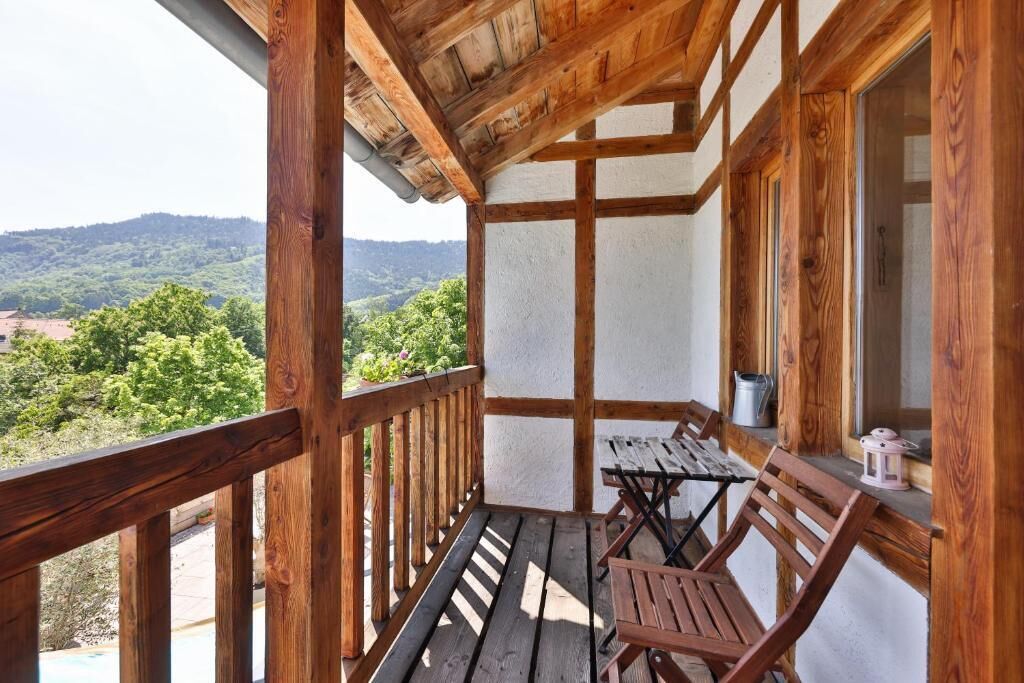 A wooden balcony with a table and chairs, overlooking a mountainous landscape.
