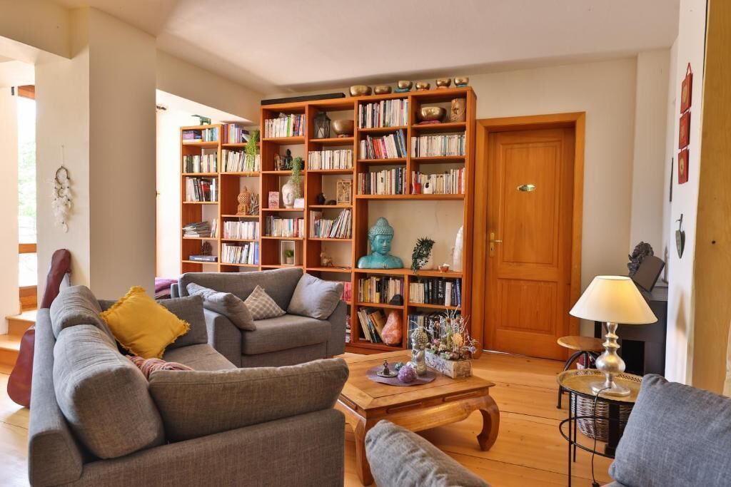 A cozy living room with a sofa, armchairs, a coffee table, and a large bookshelf filled with books and decorative items.
