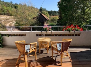 En træterrasse med fletningsmøbler og udsigt over et landligt landskab.