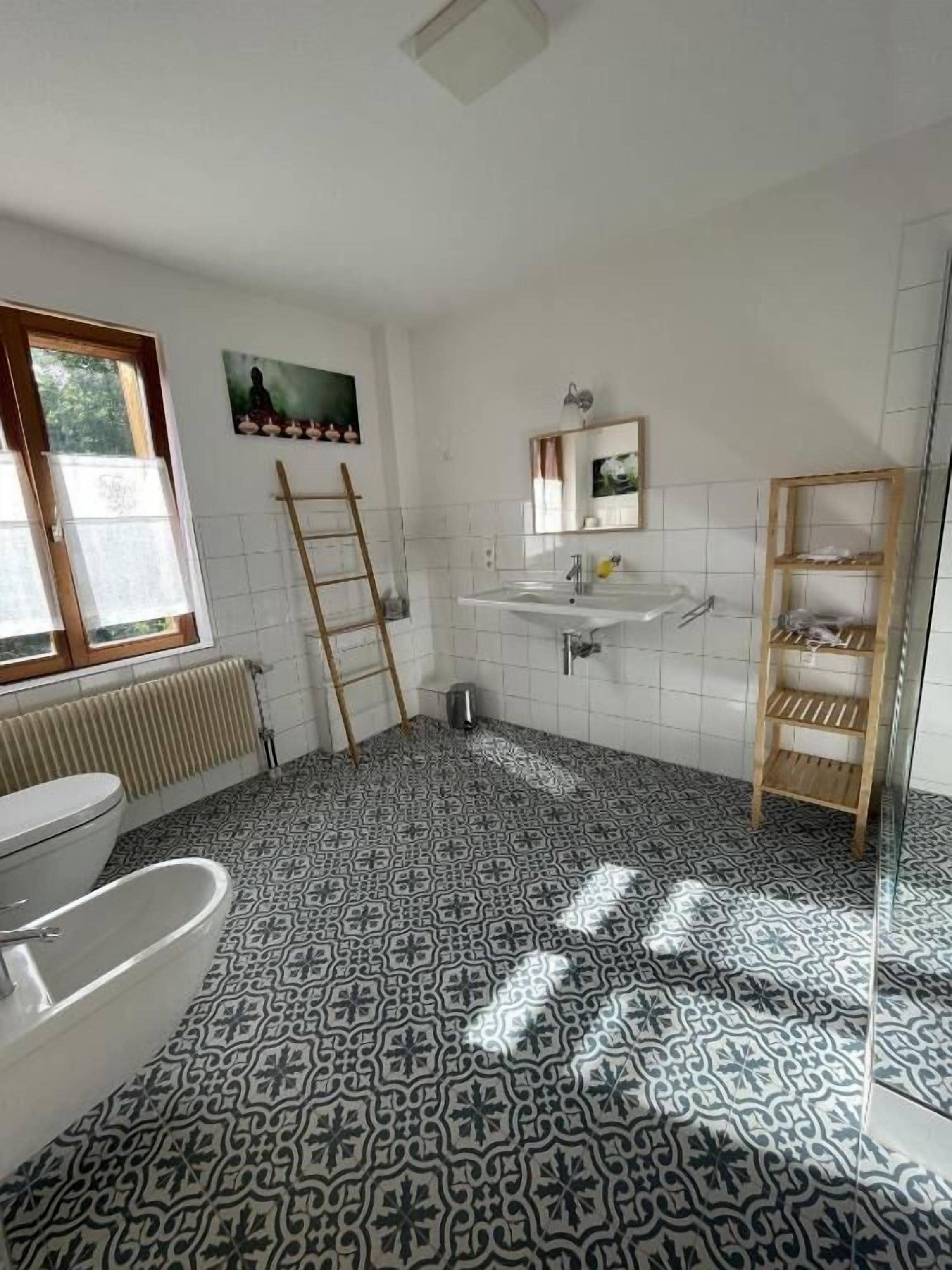 A bathroom with a patterned floor, a toilet, a sink, a mirror, and a shelf.