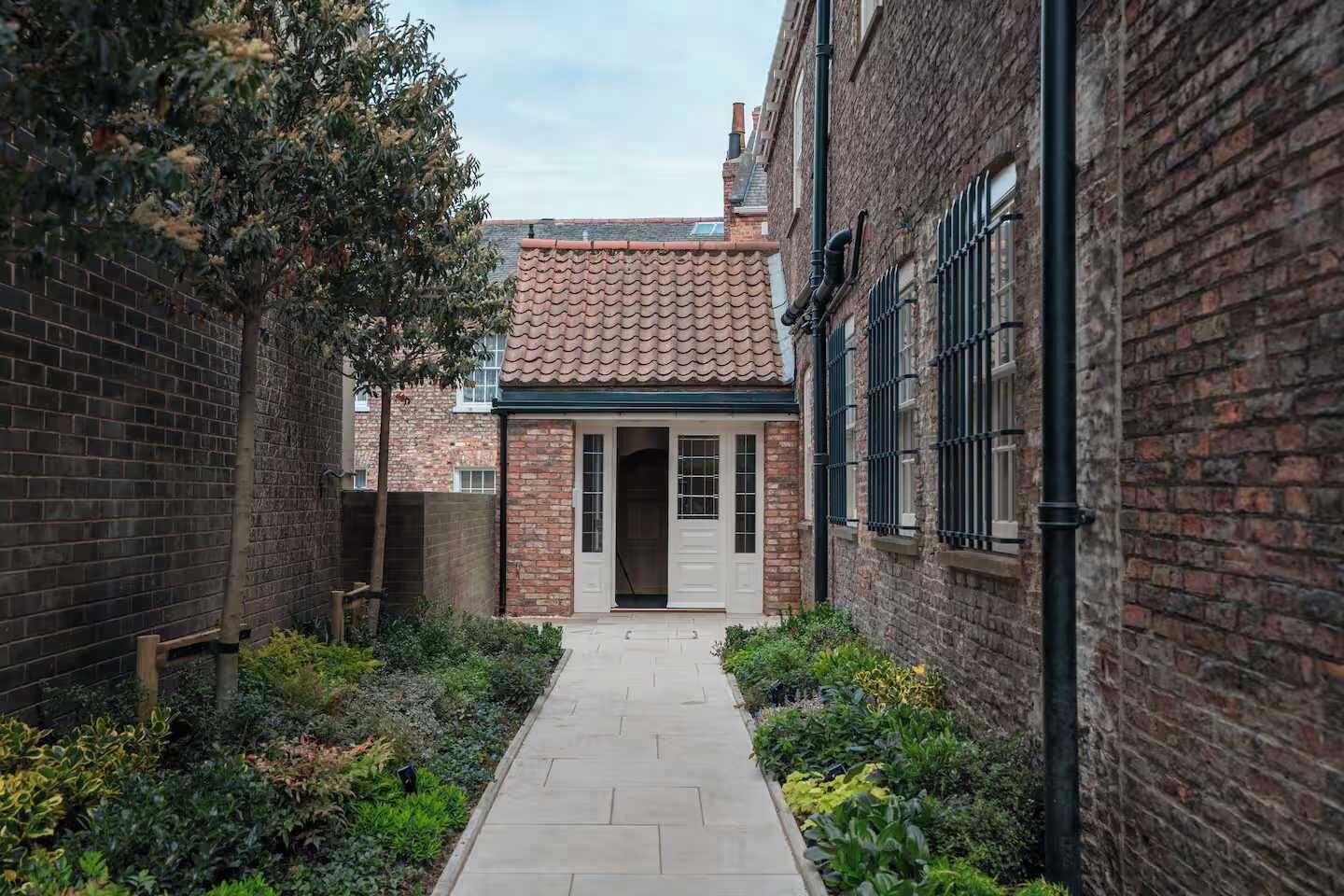 A narrow pathway leading to a building with a tiled roof and a door.