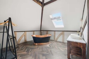 Ein Badezimmer mit freistehender Badewanne, einer Holzbank und einem Waschbecken mit Spiegel.