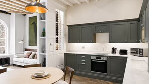 Una cocina moderna con armarios oscuros, horno empotrado y comedor con una mesa redonda y sillas.