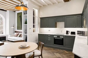 A modern kitchen with dark cabinets, a built-in oven, and a dining area with a round table and chairs. - Preacher's Yard Stylish Central York Apartment - Duplex 4 (York)