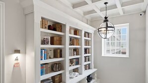 Una habitación con estanterías empotradas blancas llenas de libros y objetos decorativos, una lámpara colgante esférica y una ventana con vistas a edificios.