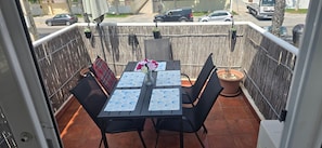 A balcony with a table set for two, chairs, a potted plant, and a view of the street. - 'Papa Luna' Apartment with Private Terrace, Wi-Fi, and Air Conditioning (Benicarló)