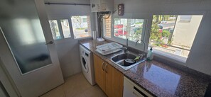 A compact kitchen with a washing machine, a sink, and a window with a view of the street. - 'Papa Luna' Apartment with Private Terrace, Wi-Fi, and Air Conditioning (Benicarló)