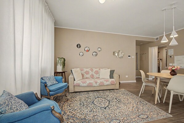 Een woonkamer met een bank, twee fauteuils, een salontafel en een eethoek met stoelen en een tafel.