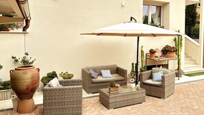 Une terrasse extérieure aménagée avec des meubles en osier, un grand parasol et des plantes en pot.