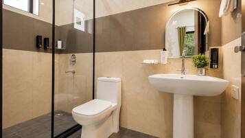 Un baño moderno con ducha de vidrio, inodoro blanco y lavamanos sobre pedestal.
