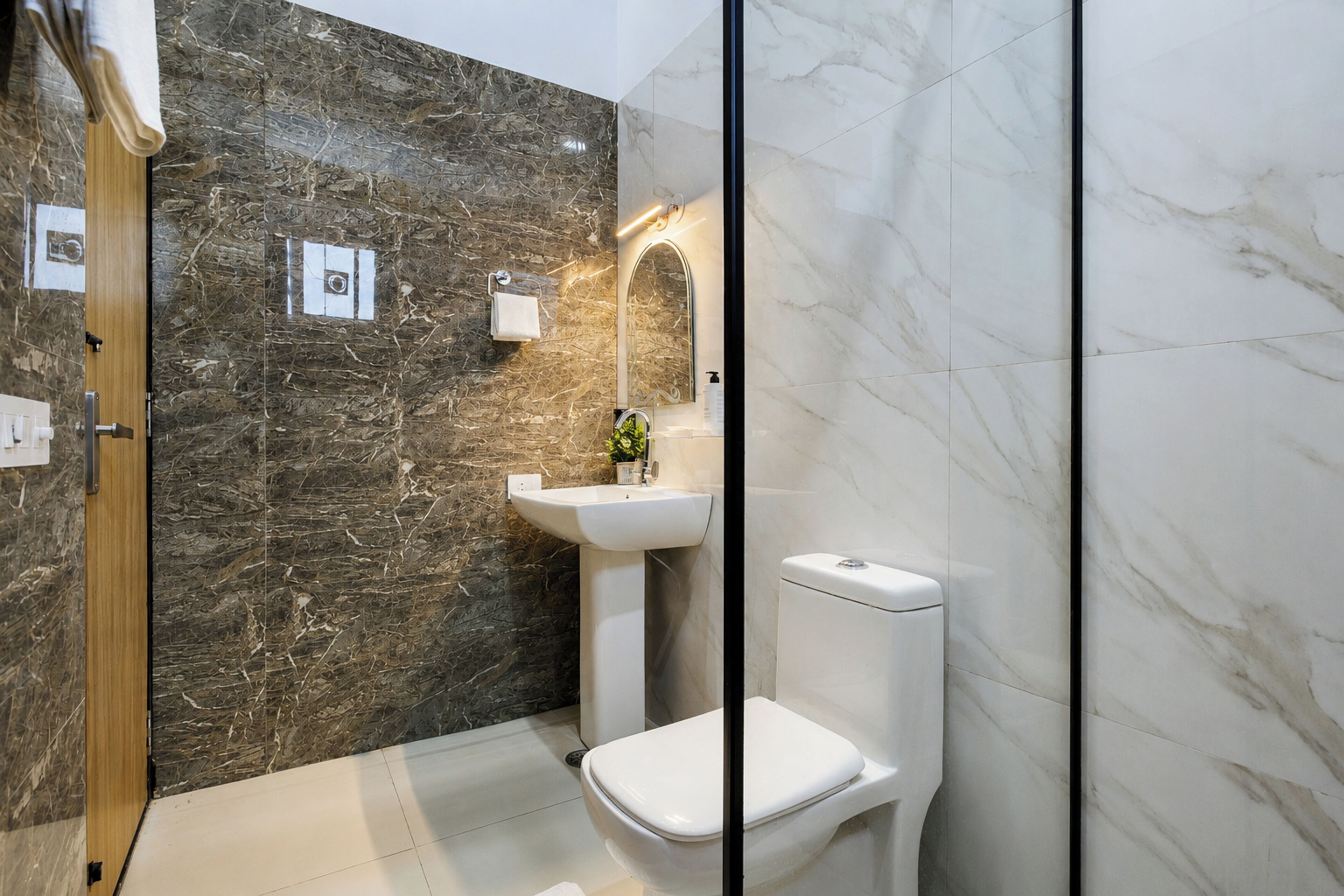 Un baño con pared de mármol, un lavamanos, un inodoro y un espejo.