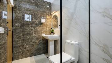 Un baño con pared de mármol, un lavamanos, un inodoro y un espejo.