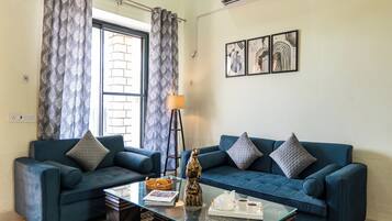 A living room with two blue sofas, a glass coffee table, a floor lamp, and a wall with abstract art.