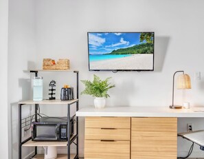 Eine moderne Küche mit Mikrowelle, Toaster und Kaffeemaschine auf einem Regal, einer Topfpflanze und einem Fernseher, der eine Strandansicht zeigt.