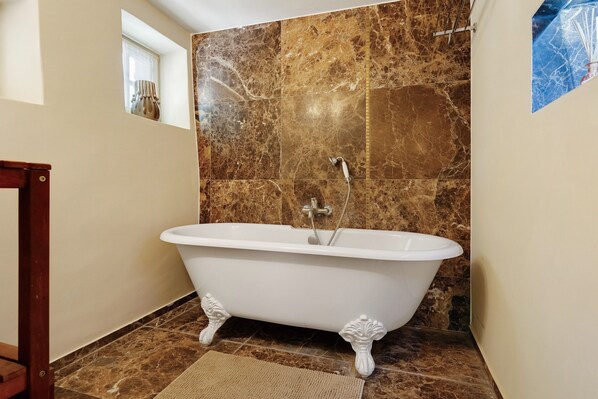 A bathroom with a freestanding bathtub, marble walls, and a wooden floor.