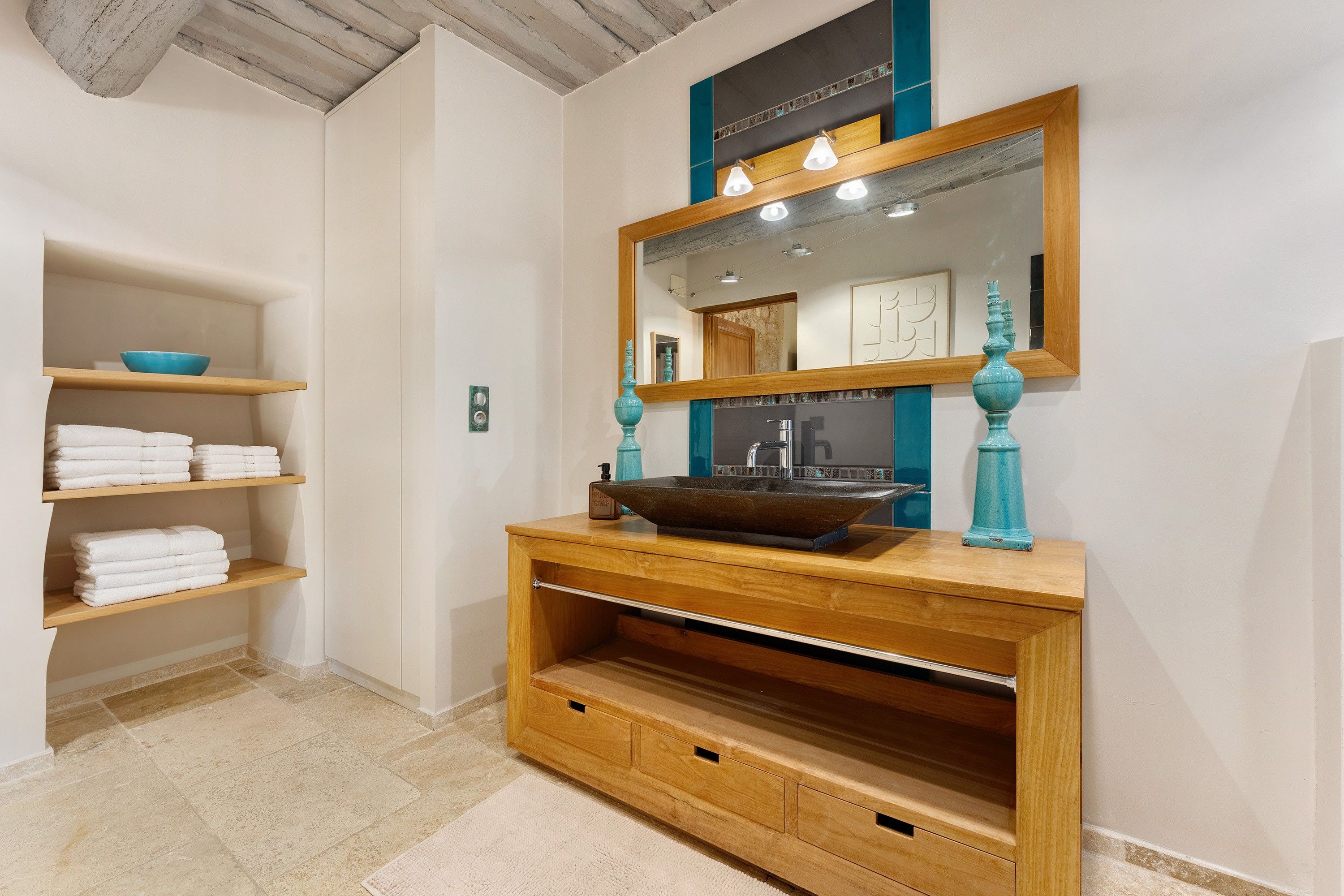 A bathroom with a wooden vanity, a large mirror, and shelves with folded towels.