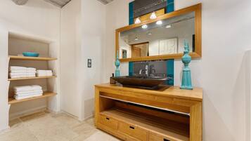 A bathroom with a wooden vanity, a large mirror, and shelves with folded towels.