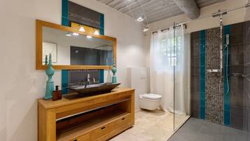 Un baño moderno con tocador de madera, un espejo grande, lavabo sobre encimera, inodoro y cabina de ducha con mampara de vidrio.