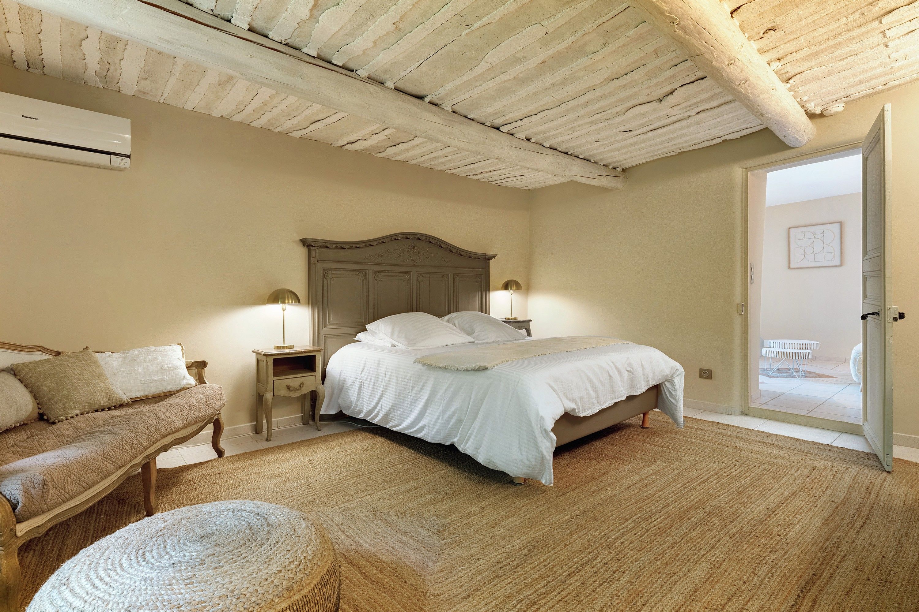 Quarto com cama, mesas de cabeceira, luminária, cadeira e porta para área externa.