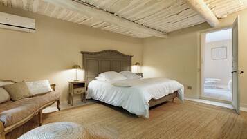 Quarto com cama, mesas de cabeceira, luminária, cadeira e porta para área externa.