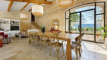 Un comedor amplio con una mesa grande y sillas, una cocina al fondo y vistas a través de un ventanal.