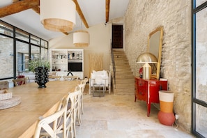A spacious dining area with a wooden table and chairs, a kitchen in the background, and a staircase leading to an upper level.