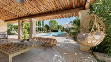 A covered outdoor area with a pool, lounge chairs, and a hanging chair.