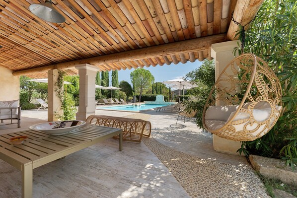 A covered outdoor area with a pool, lounge chairs, and a hanging chair.
