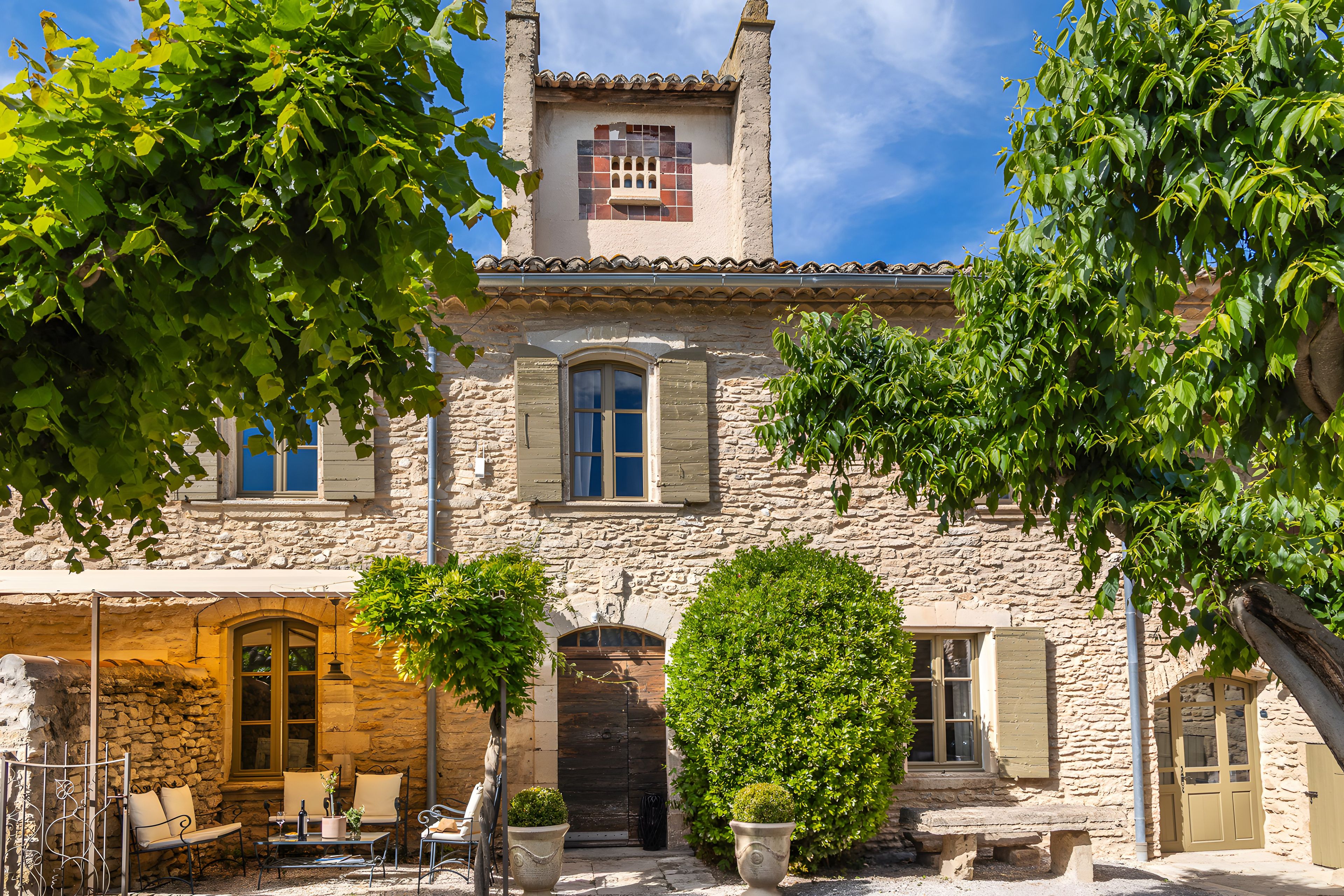 A stone building with a tiled roof, a bell tower, and a courtyard with seating and greenery.