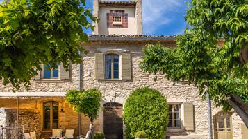 A stone building with a tiled roof, a bell tower, and a courtyard with seating and greenery.