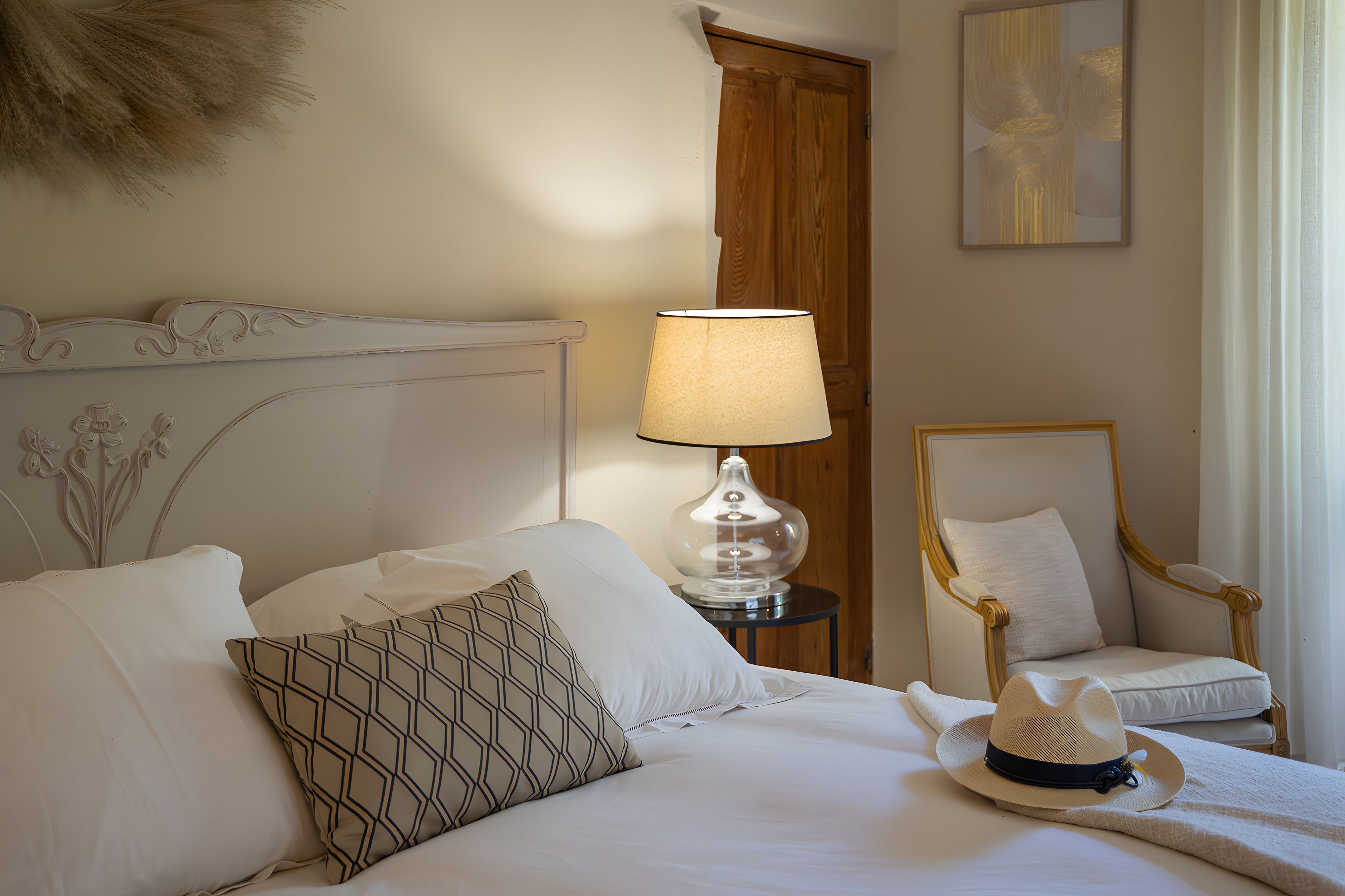 Quarto de hotel com uma cama, uma luminária, uma cadeira e um detalhe decorativo na parede.