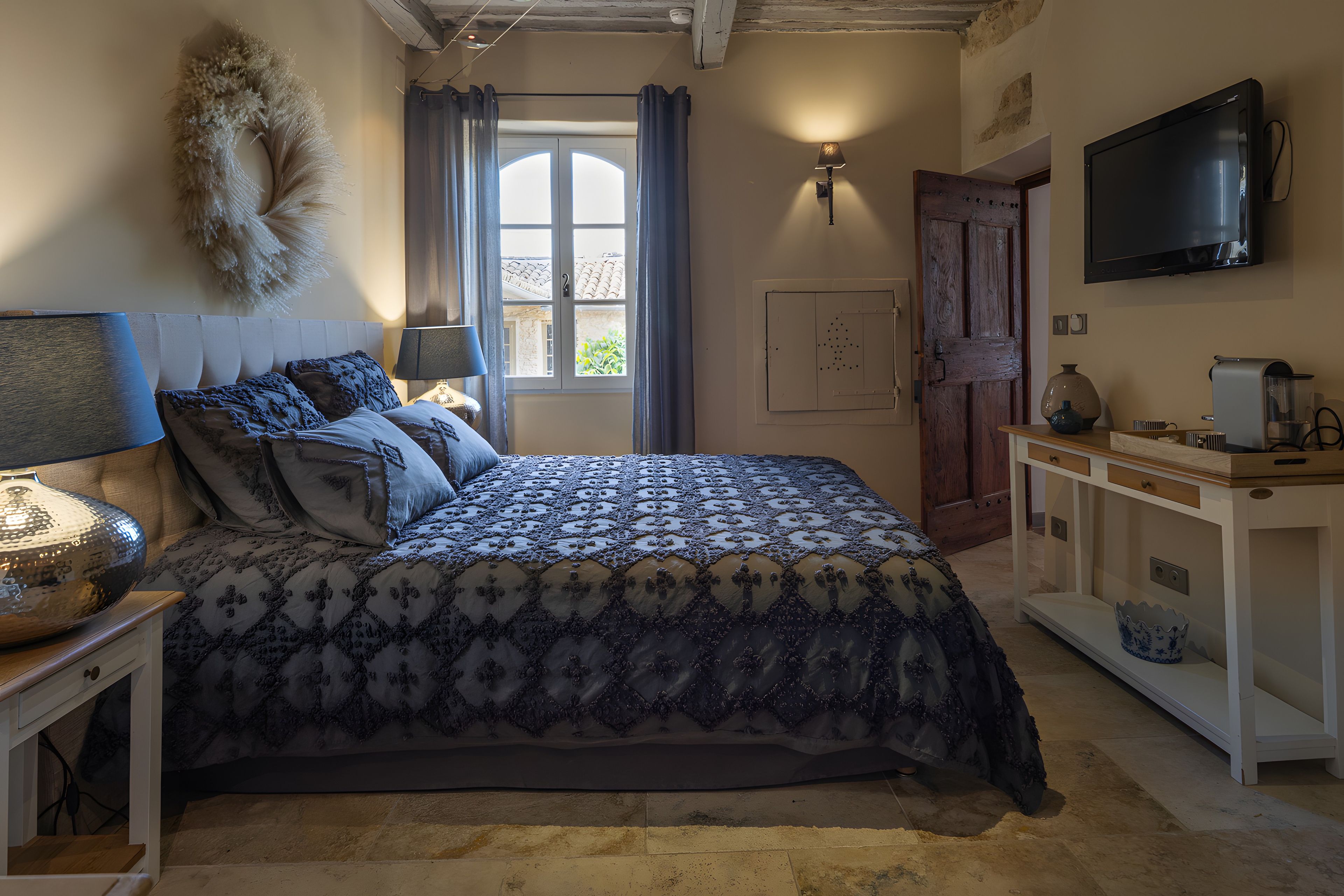 A bedroom with a bed, bedside table, lamp, and a TV on the wall.