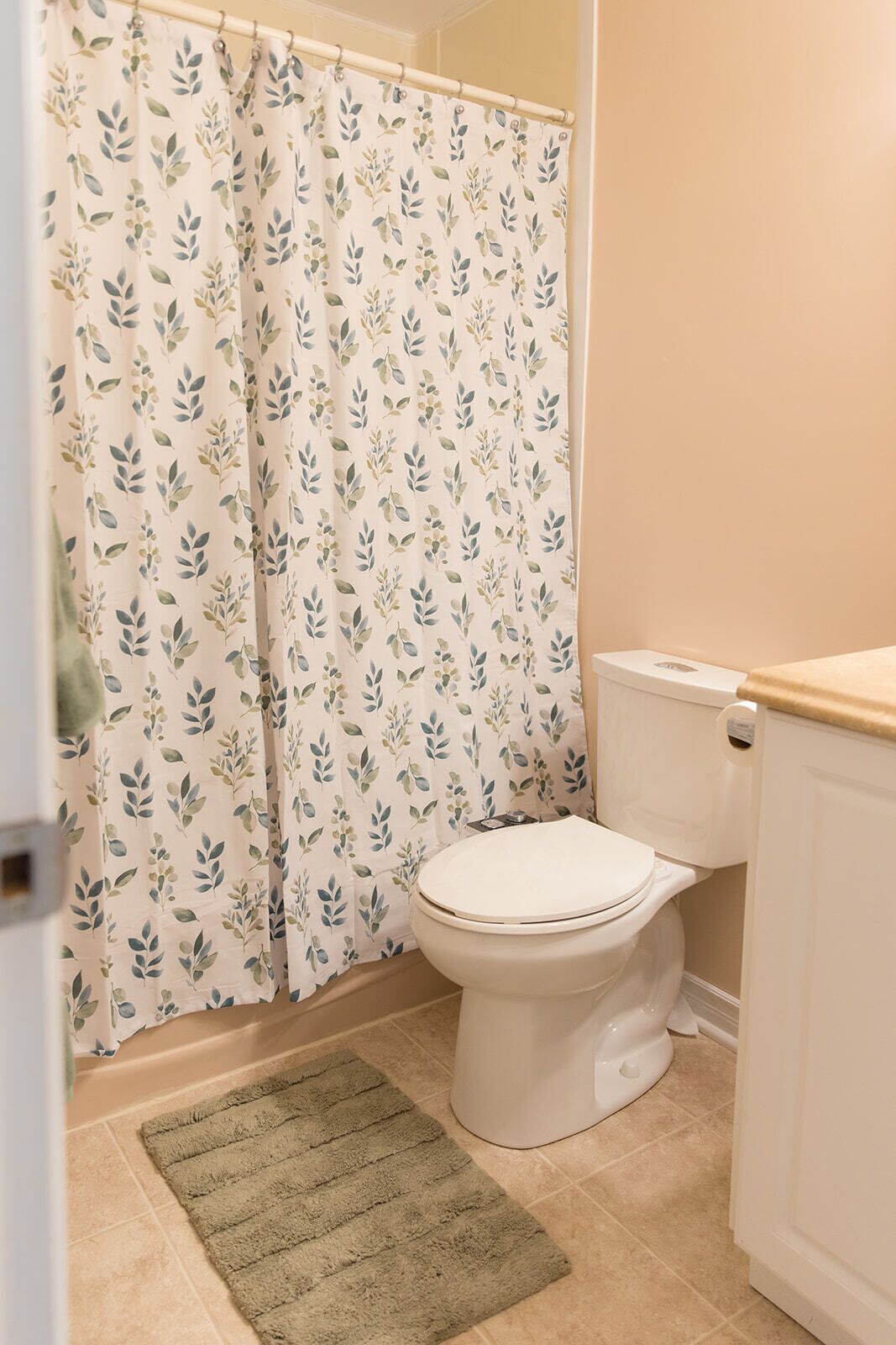Een badkamer met toilet, douchegordijn met bladmotief en een groene mat.