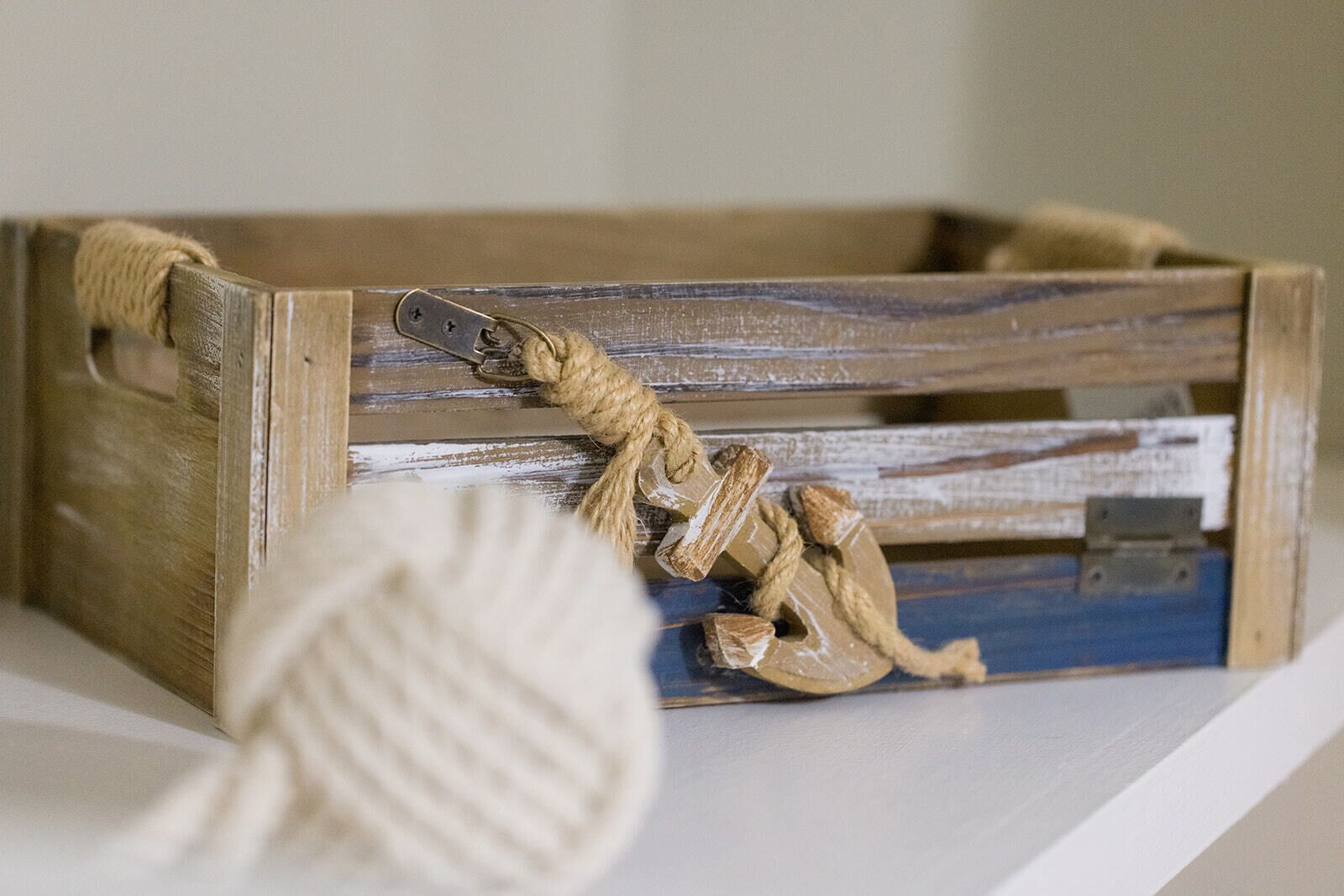 A rustic wooden crate with a rope handle and a decorative figure.