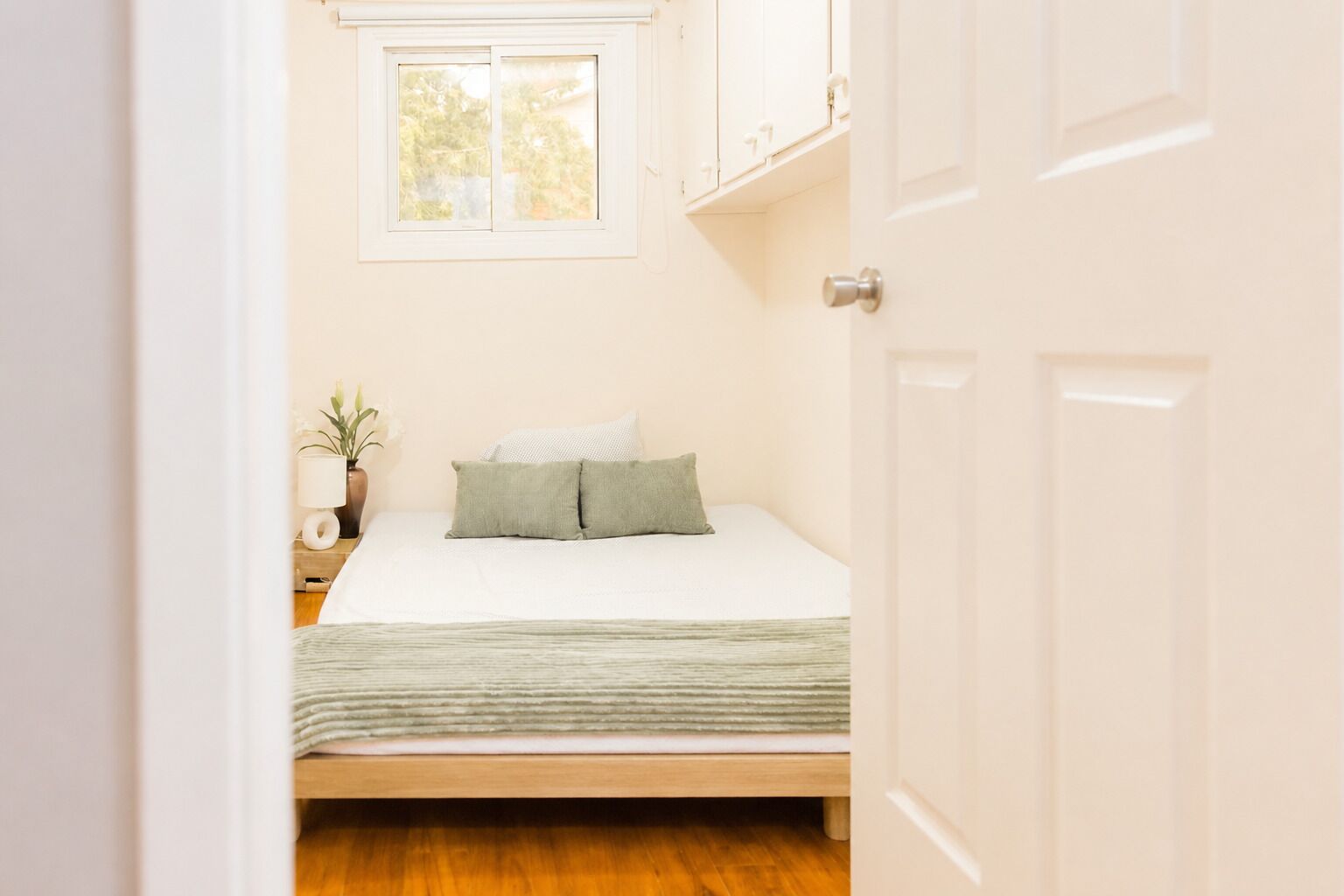 Quarto com uma cama de solteiro, mesa de cabeceira, abajur e janela.