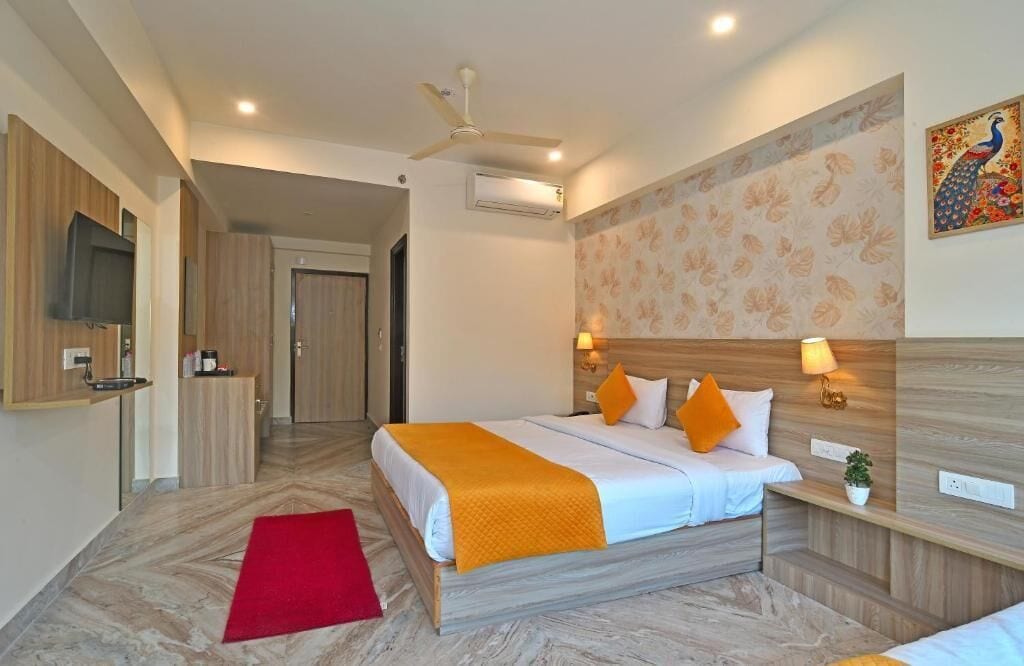 Habitación de hotel con cama, televisión, ventilador de techo y alfombra roja.
