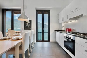 A modern kitchen with a dining area, large windows, and a view of the sea.