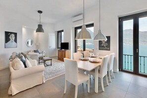 A modern living room with a dining area, white furniture, and a view of the sea.