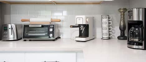 A kitchen with a toaster, a coffee maker, a rolling pin, and a coffee machine.